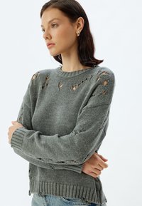 Grijze gebreide trui met versleten details, ronde hals, geribbelde manchetten en onderrand, textuurstof en een relaxed fit.