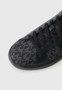 Baskets noires avec un motif texturé, dotées de lacets noirs, d'une tige en cuir lisse et d'une semelle en caoutchouc. Accents de logo visibles.