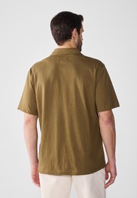 Kortärmad polo skjorta i olivgrön bomull med avslappnad passform, mjuk textur och enkel kragsdesign.