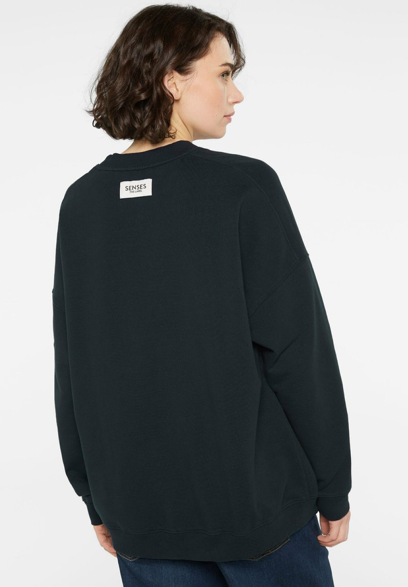 Dunkelgrünes, übergroßes Sweatshirt mit Rundhalsausschnitt, gerippten Bündchen und Saum. Verfügt über ein Branding-Etikett am oberen Rückenausschnitt. Weicher, strukturierten Stoff.