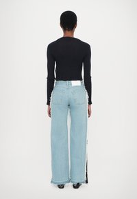 Camiseta negra de manga larga con tejido acanalado combinada con vaqueros de pierna ancha en azul claro, con bordes deshilachados y una etiqueta blanca en la parte trasera.