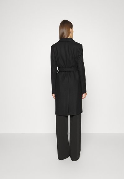 Black belted coat with a structured collar and long sleeves, featuring a smooth texture and a tailored fit, paired with wide-leg black trousers.