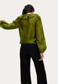 Groene zijden blouse met een geplooide kraag en pofmouwen. Draagt met high-waisted zwarte jeans. Gladde textuur en vloeiend ontwerp.