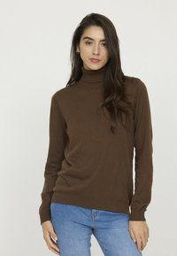 Un pull-over col roulé marron en tissu tricoté doux, avec des manches longues, des poignets et un ourlet côtelés, associé à un jean bleu clair.