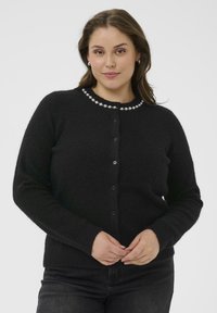 Cardigan noir à boutonnière fabriqué en tissu doux et texturé, avec une finition décorative en perles autour du col et des poignets côtelés.