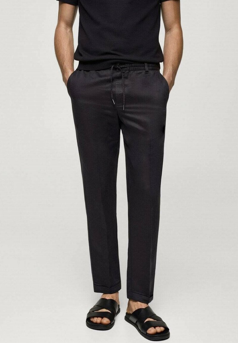 Zwarte, slim-fit broek met een elastische tailleband en trekkoord, gemaakt van gladde stof met taps toelopende benen, gecombineerd met zwarte sandalen.