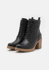 Stivaletti in pelle nera con punta rotonda, tacco squadrato chunky color tan e lacci frontali. Presentano una linguetta sul retro e una suola testurizzata.