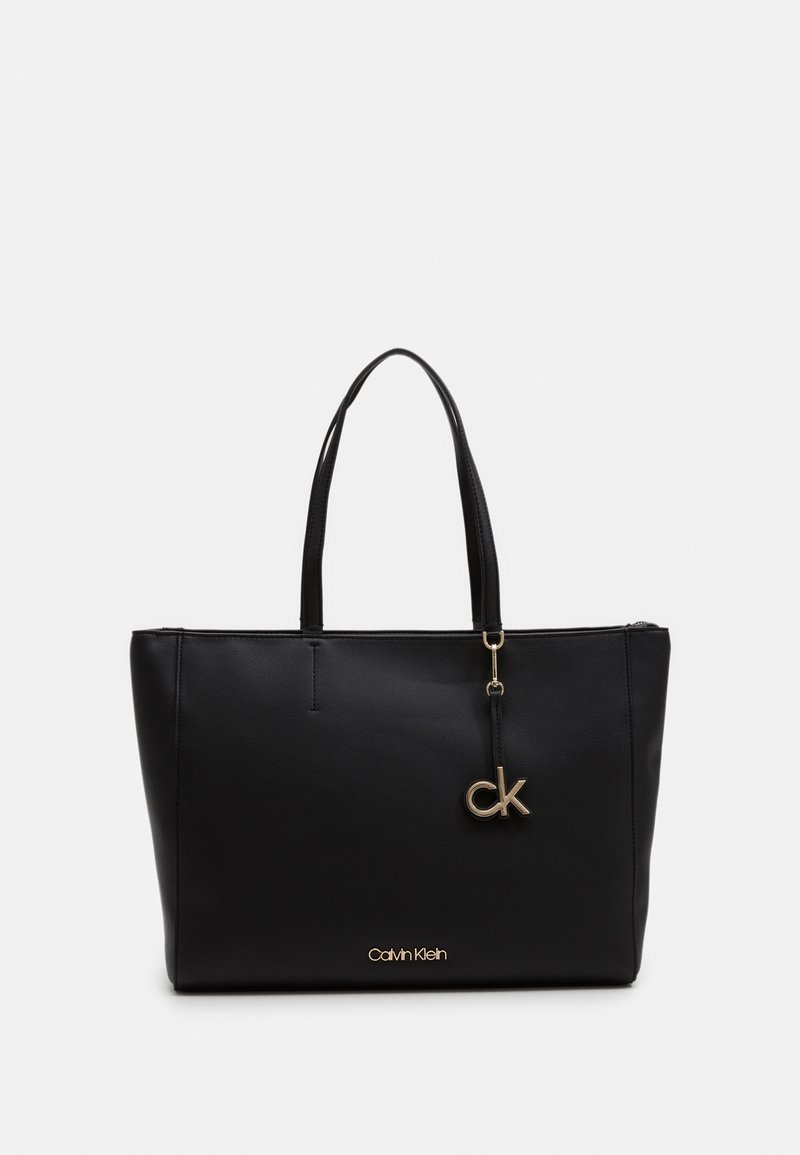 Sac fourre-tout noir Calvin Klein en simili cuir lisse, doté de deux poignées, d'un charm logo doré et d'une fermeture éclair sur le dessus.