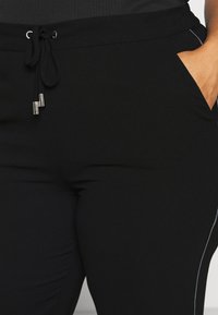 Zwarte joggers met een trekkoord in de taille, voorzien van zilveren accenten en zijzakken, gemaakt van een gladde, elastische stof.