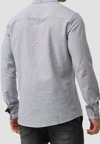 Jasnoszara koszula z długim rękawem, kołnierzykiem zapinanym na guziki oraz mankietami na guziki, wykonana z gładkiej, strukturalnej tkaniny, z zaokrąglonym dołem.