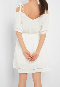 Abito bianco con maniche corte, design off-the-shoulder, vita elastica e bordatura in pizzo all'orlo e alle maniche. Spalline regolabili.