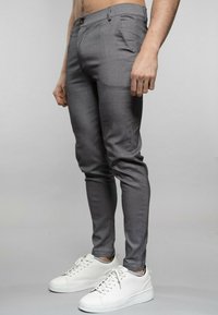 Pantalons gris ajustés en tissu lisse, avec des poches avant et une fermeture à bouton, associés à des baskets blanches.
