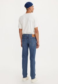 Jeans de mezclilla en un azul medio con un corte recto, que presentan un parche de cuero marrón en la parte trasera de la cinturilla y sutiles detalles de desgaste.