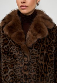 Cappotto in pelliccia sintetica con motivo leopardato marrone, dotato di un colletto morbido marrone e una finitura testurizzata, progettato in una forma oversize.