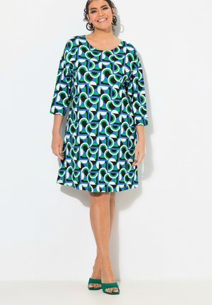 Robe à manches courtes avec un motif géométrique en vert, bleu, noir et blanc. Coupe en A avec un col rond et une longueur au genou.