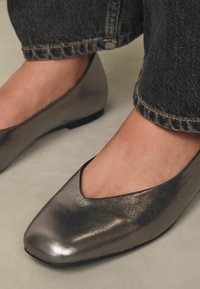 Bailarinas gris metálico con diseño en corte en V, acabado suave y tacón bajo. Suela negra y detalles de costura mínimos visibles.