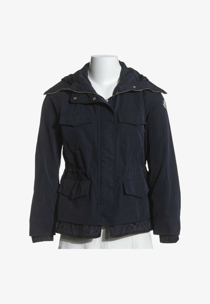 Veste à capuche bleu marine avec fermeture éclair frontale, quatre poches à rabat, poignets élastiques et écusson avec logo sur la manche gauche supérieure.