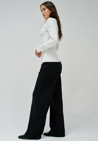 Witte geribbelde top met lange mouwen gecombineerd met zwarte wijde broek. De top heeft accentknopen op de mouwen, wat zorgt voor een textuurrijke uitstraling.