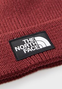 Close-up of burgundy knitted fabric with a black and white "The North Face" logo patch sewn on the surface.