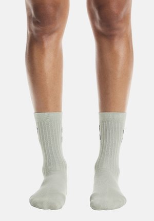 Des chaussettes vert clair côtelées, ajustées parfaitement, arborant un logo noir sur le côté extérieur. Le matériau semble doux avec une finition texturée.