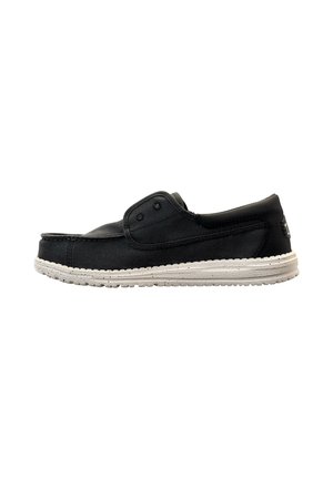 Zwarte casual slip-on schoen met witte gestructureerde rubberen zool, canvas bovenwerk en ventilatieoogjes, zijaanzicht op witte achtergrond.