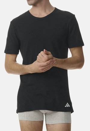 Schwarzes Baumwoll-T-Shirt mit Rundhalsausschnitt und kurzen Ärmeln. Mit einem weißen Adidas-Logo unten rechts. Getragen mit grauen Shorts.