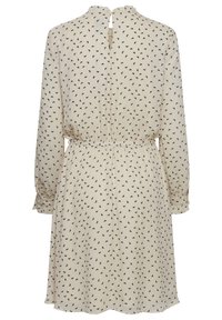 Robe beige à motif de feuilles noires, manches longues, taille élastique, dos avec ouverture en forme de goutte, et poignets froncés. Tissu lisse avec une coupe fluide.