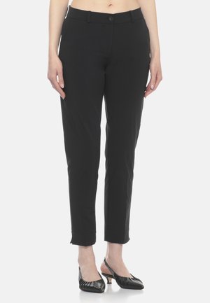 Pantaloni aderenti neri alla caviglia indossati da una persona in piedi, abbinati a scarpe slingback nere con tacco basso.