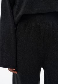 Czarny dzianinowy komplet do wypoczynku o błyszczącej fakturze; długie rękawy i elastyczny pas. Materiał wydaje się miękki i elastyczny, zaprojektowany z myślą o komforcie.