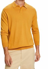 Gelbes Langarm-Polo-Shirt mit weicher Textur, drei-knöpfiger Knopfleiste und gerippten Bündchen, kombiniert mit hellbeigen Hosen.