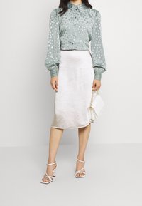 Mintgrøn bluse med hvid leopardprint, pufærmer og knapper; parret med en skinnende lys grå satin midi-nederdel og hvide hæle.