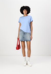 Tricou bleu deschis cu mânecă scurtă, fustă din denim decolorat, geantă roșie, adidași albi și șosete albe. Stil contemporan casual.