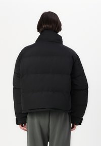 Svart pufferjakke med høy krage og quiltet design. Jakken har en cropped passform med brede ermer og en jevn tekstur.