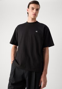 T-shirt di cotone nera con colletto a girocollo, maniche corte e un sottile logo ricamato sul petto, abbinata a pantaloni neri.