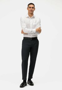 Witte lange mouwen shirt met knopen en een borstzak, gecombineerd met op maat gemaakte donkere broek en zwarte schoenen, wat zorgt voor een gestructureerde uitstraling.
