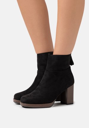 Botas de tobillo de ante negro con un tacón grueso de bloque, punta redondeada y un diseño de puño doblado. Incluye un tacón de madera texturizada.