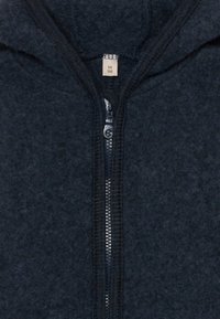 Marineblaue Kapuzenjacke mit Reißverschluss aus strukturiertem Fleece-Material. Mit einem Reißverschluss in der Mitte vorne und einer Kapuze, versehen mit einem Stoffetikett, das die Größe 56 1M angibt.