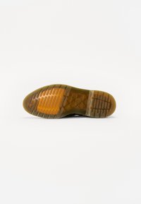 Suola di scarpa in gomma con battistrada a motivo, caratterizzata da un'area traslucida, prevalentemente in tonalità marroni e arancioni, con scanalature ben visibili.