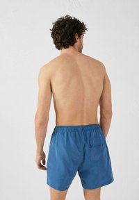 Pantaloni da bagno blu con cinturino elastico in vita e tasca posteriore, realizzati in tessuto liscio. Design semplice senza motivi o grafiche.