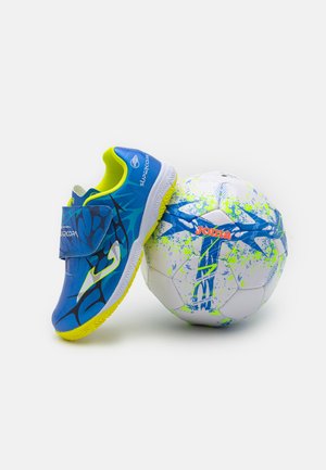 Zapatos de fútbol azules con una correa de velcro, suela de goma texturizada y acentos en amarillo neón al lado de una pelota blanca con un diseño de manchas azules y verdes.