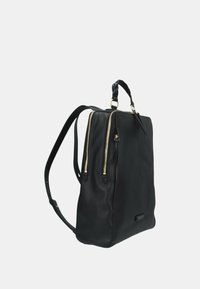 Zaino in pelle nera con doppie zip dorate, superficie texturizzata, impugnatura superiore e spallacci regolabili. Forma rettangolare con base piatta.