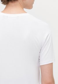 T-shirt bianca in cotone con colletto a girocollo, maniche corte e una superficie liscia. La vista posteriore non mostra loghi né motivi.