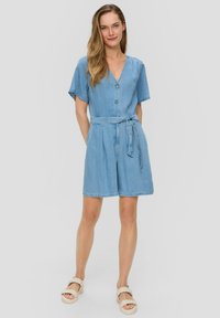 Combinaison en denim bleu clair avec des manches courtes, fermeture à boutons à l'avant, décolleté en V, taille cintrée avec un lien, et shorts amples.