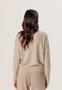 Beige kasjmier trui, relaxte pasvorm, geribbelde manchetten en onderkant, zachte textuur, ronde halslijn, achterkant. Gecombineerd met bijpassende beige broek.