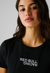 Schwarzes, geripptes T-Shirt mit einem weißen gestickten "RED BULL RACING"-Logo auf der Brust. Schlichtes Rundhalsausschnitt-Design.