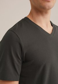Sötét grafit szürke v-nyakú póló, amely puha pamutból készült, rövid ujjaival és sima textúrájával, minimális varrással.
