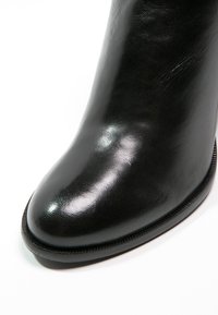 Botte en cuir noir avec un bout arrondi et des coutures visibles le long de la semelle, présentée sur un fond blanc.