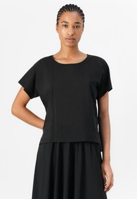 Haut noir à manches courtes avec un col rond et une coupe lâche. Fait en tissu lisse avec une finition mate. Design simple, sans motifs.