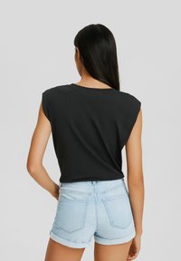 Camiseta sin mangas negra con cuello redondo, combinada con pantalones cortos de mezclilla azul claro con dobladillos enrollados y bolsillos traseros.