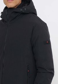 Schwarze wattierte Jacke mit hohem Kragen und verstellbarer Kapuze, ausgestattet mit Reißverschlusstaschen und einem Logoaufnäher am Ärmel. Glatte Textur.